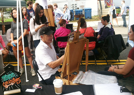 Mark drawing at the festival with a line of people behind him waiting to get their caricature!